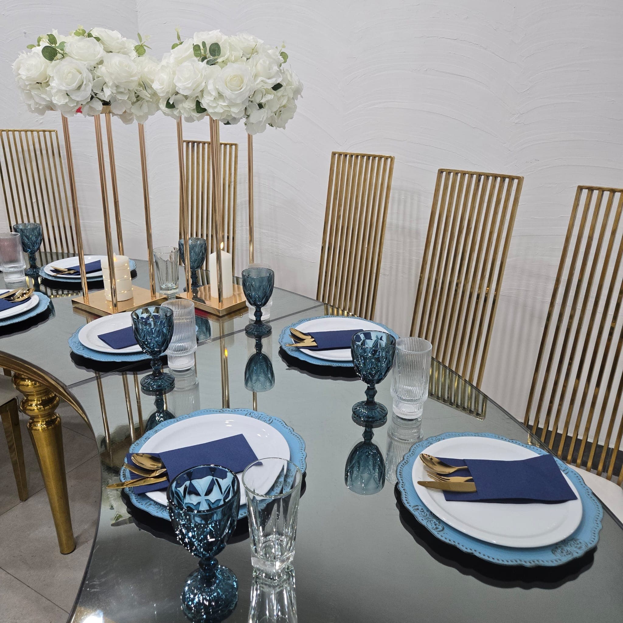 Banquet table with a mirrored top, gold chairs, and blue place settings.