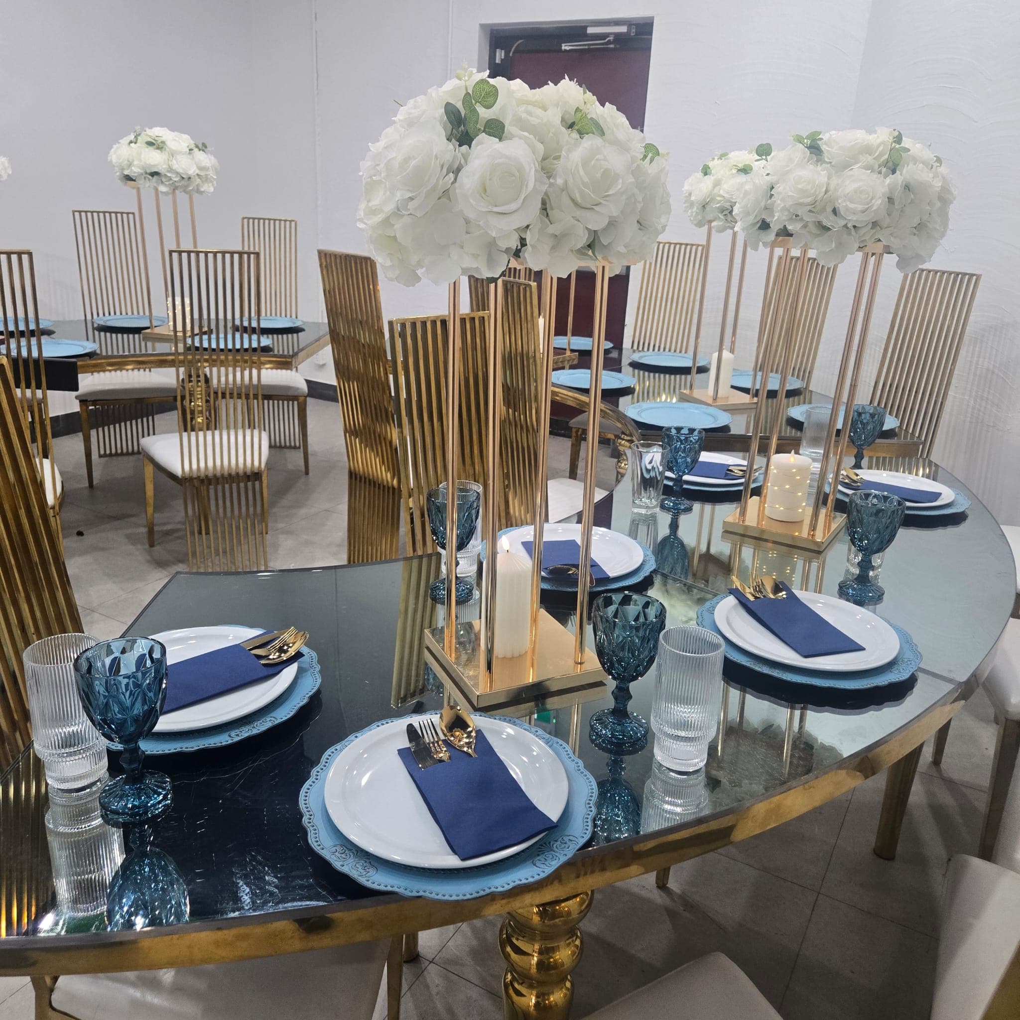 Close-up of blue and gold table setting with white rose centerpieces.