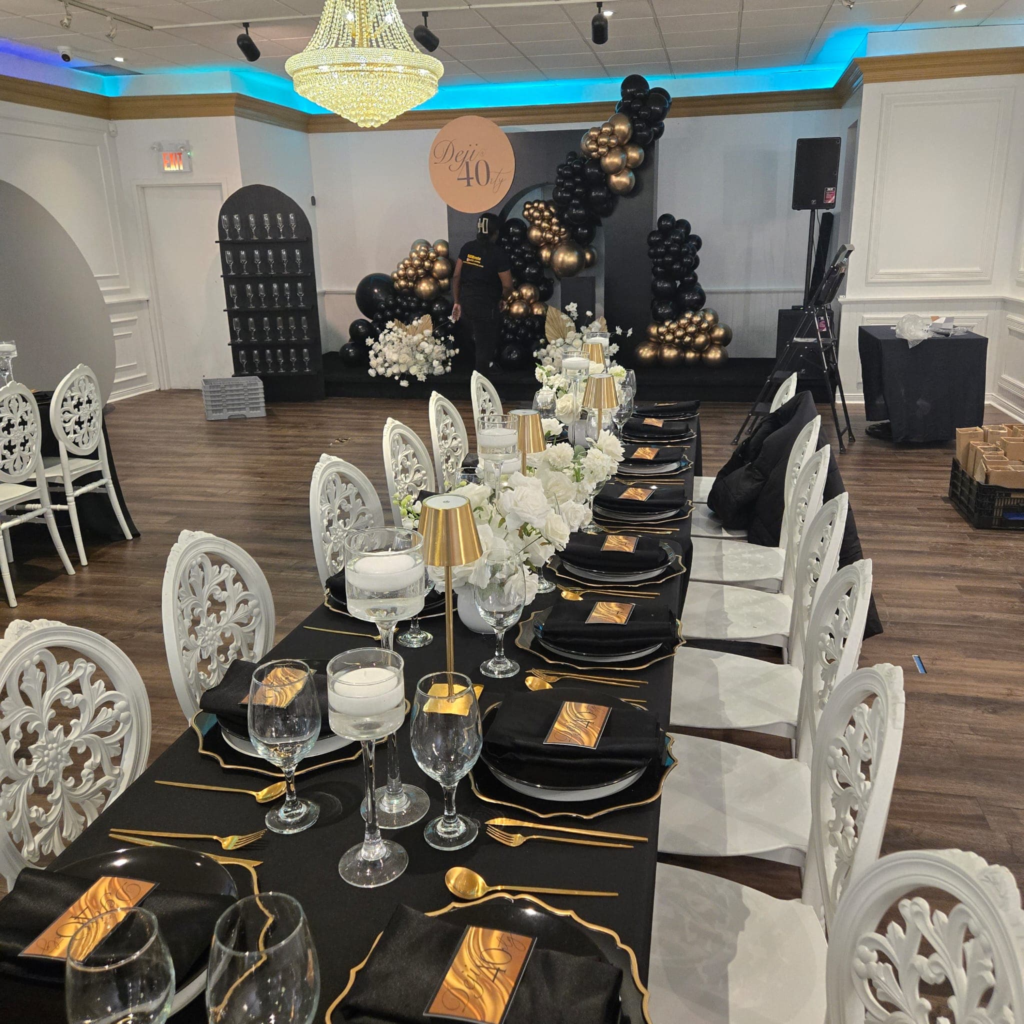 Banquet hall dressed for a 40th birthday — black and gold balloon arch, long tables, ornate white chairs.