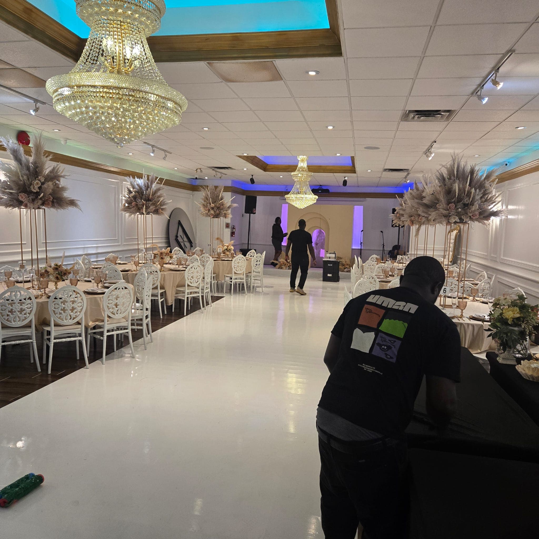 Banquet hall interior with a white dance floor, twin chandeliers, and pampas grass centrepieces.