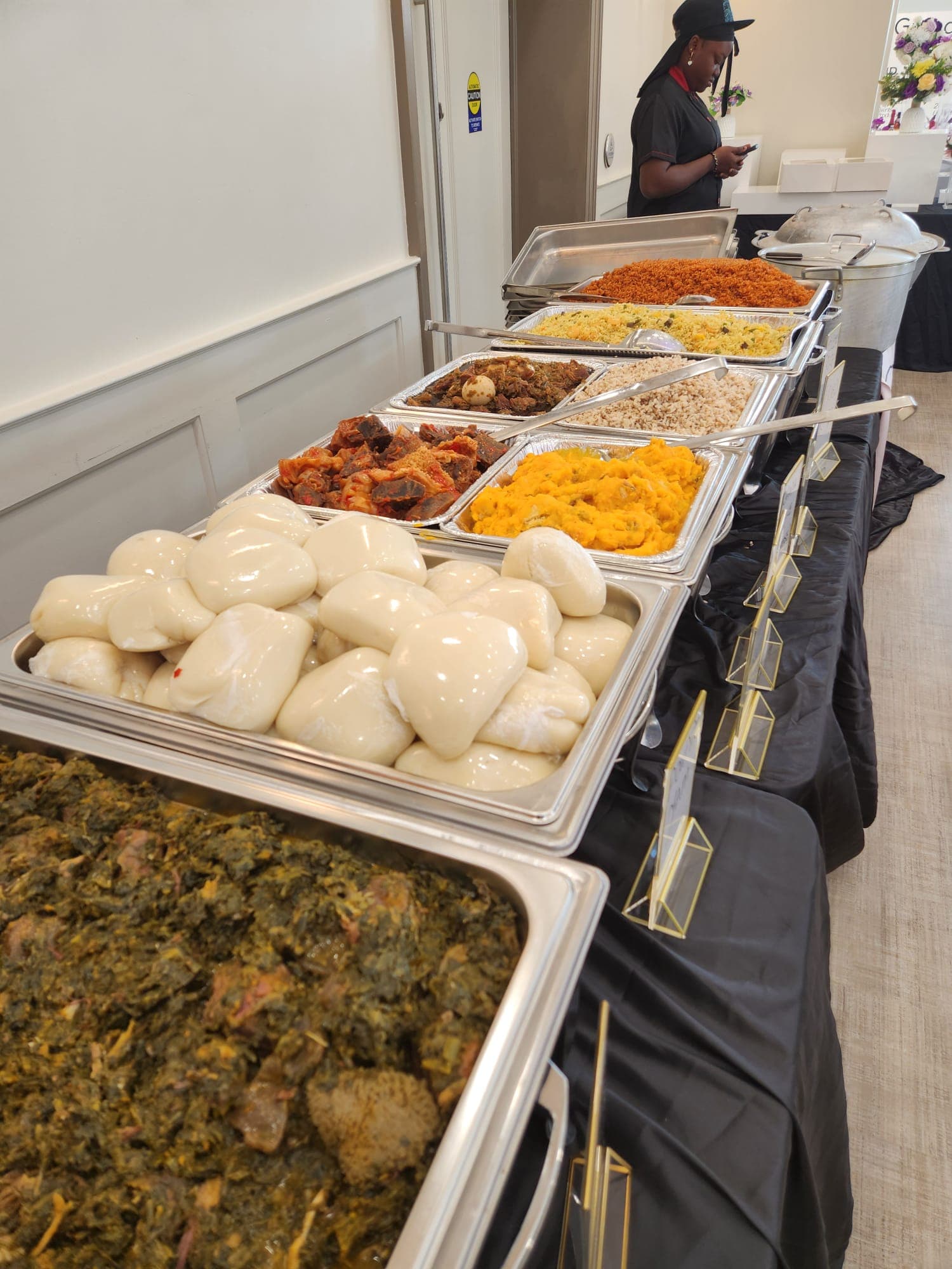 Full Nigerian buffet spread with fufu, egusi, jollof, and assorted rice in chafing dishes.