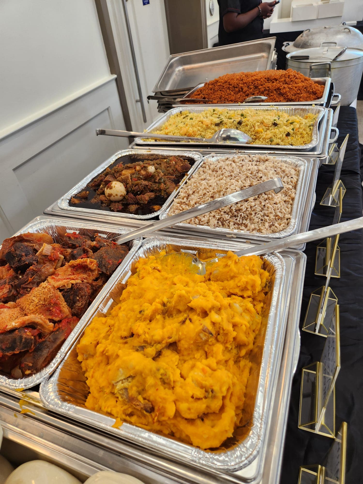 Close-up of catering trays with yam pottage, oxtail, and brown rice.
