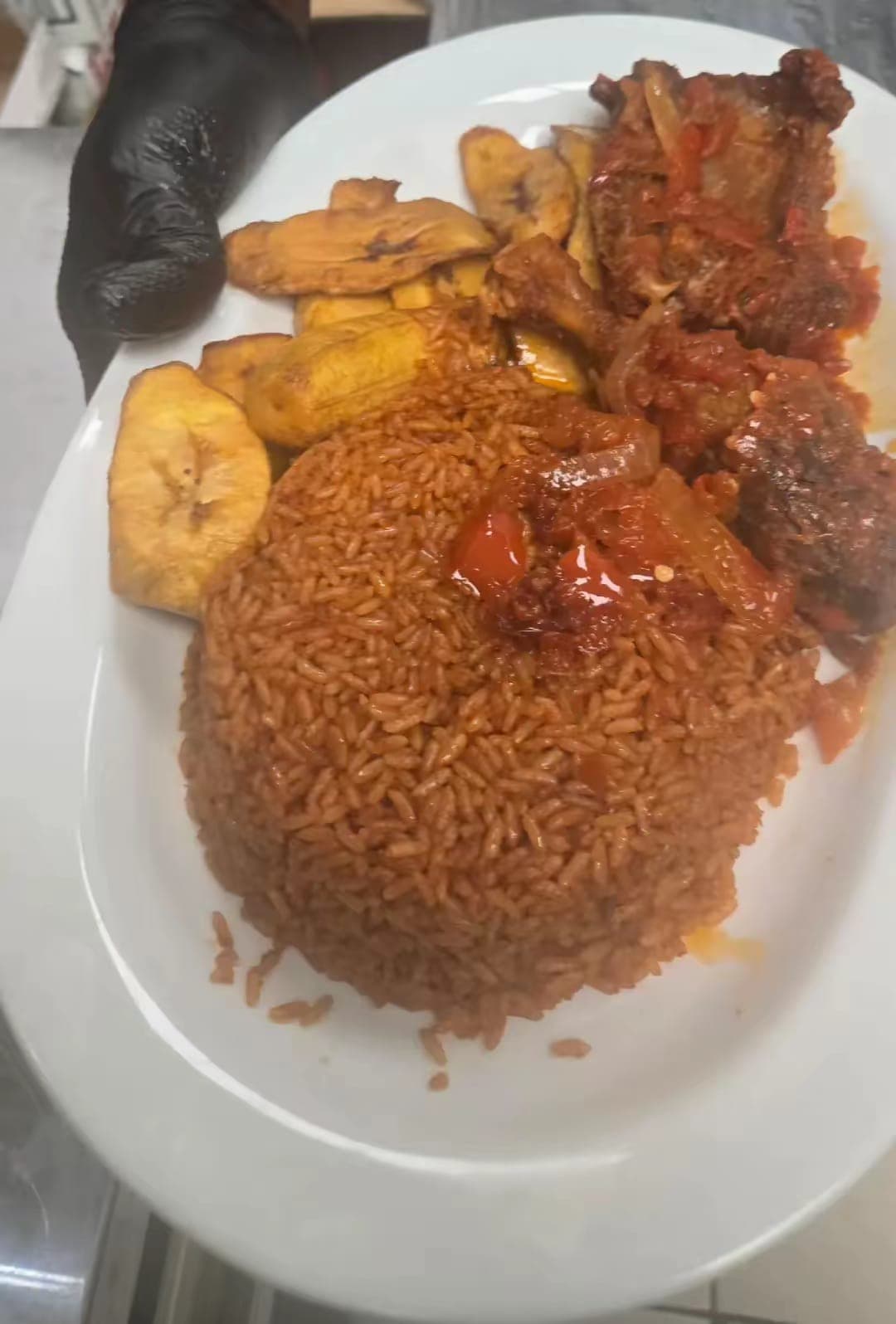Plate of smoky party jollof rice with fried plantain and stewed meat in pepper sauce.
